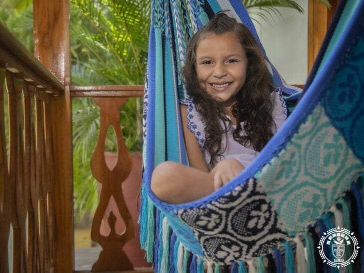 hamac chaise de luxe XL, fabriqué en Colombie, blanche et bleue avec une petite fille à l'intérieur du hamac chaise. Vue de coté
