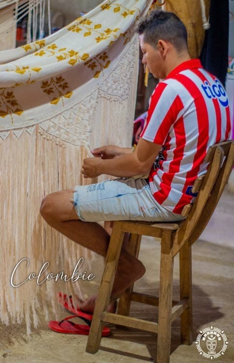 photo d'un artisan de Colombie, assis, qui tisse les franges en macramé d'un hamac