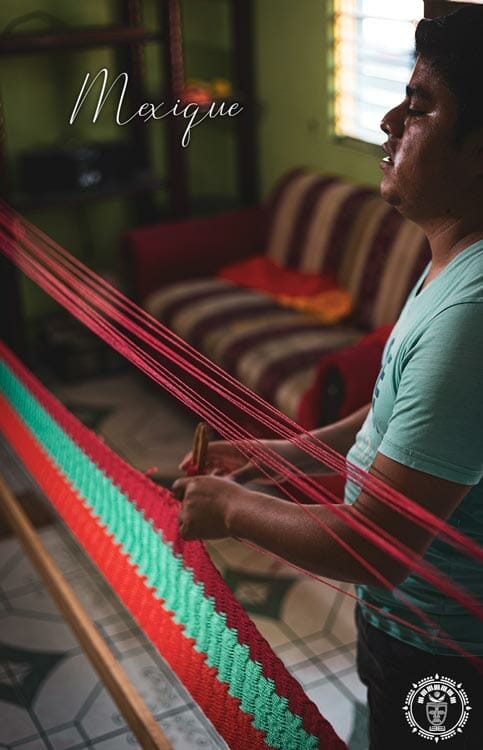 Une tisserand mexicain qui tisse un hamac vert et rouge sur un métier à tissé, vue de profil