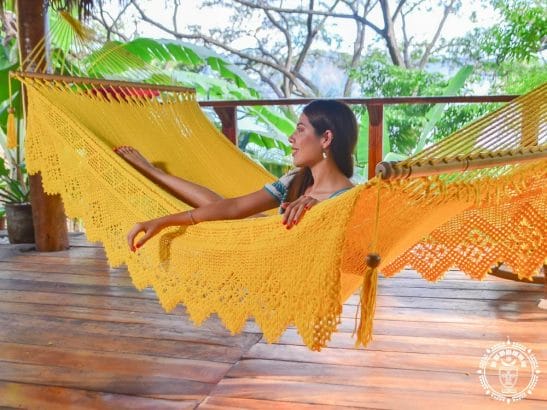 hamac à barre de luxe du Nicaragua en coton L, couleur jaune, vue de coté avec une femme couchée qui regarde sur la gauche