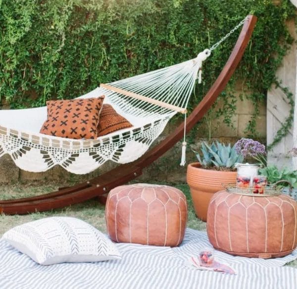 bar hamac dans un jardin avec des éléments décoratifs tels que : coussins, tapis et un petit support pour les objets