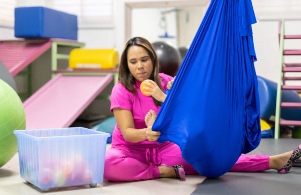 Découvrez le hamac thérapeutique et la méthode Padovan - Photo d'une ergothérapeute avec un enfant dans un hamac bleu pour une séance comportementale.