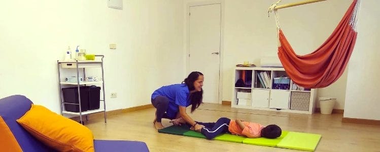Pour qui est la méthode PADOVAN - seance comportementale dans le cabinet d'un ergothérapeute avec un jeune enfant faisant des exercice d'assouplissement par terre, a coté un hamac chaise.